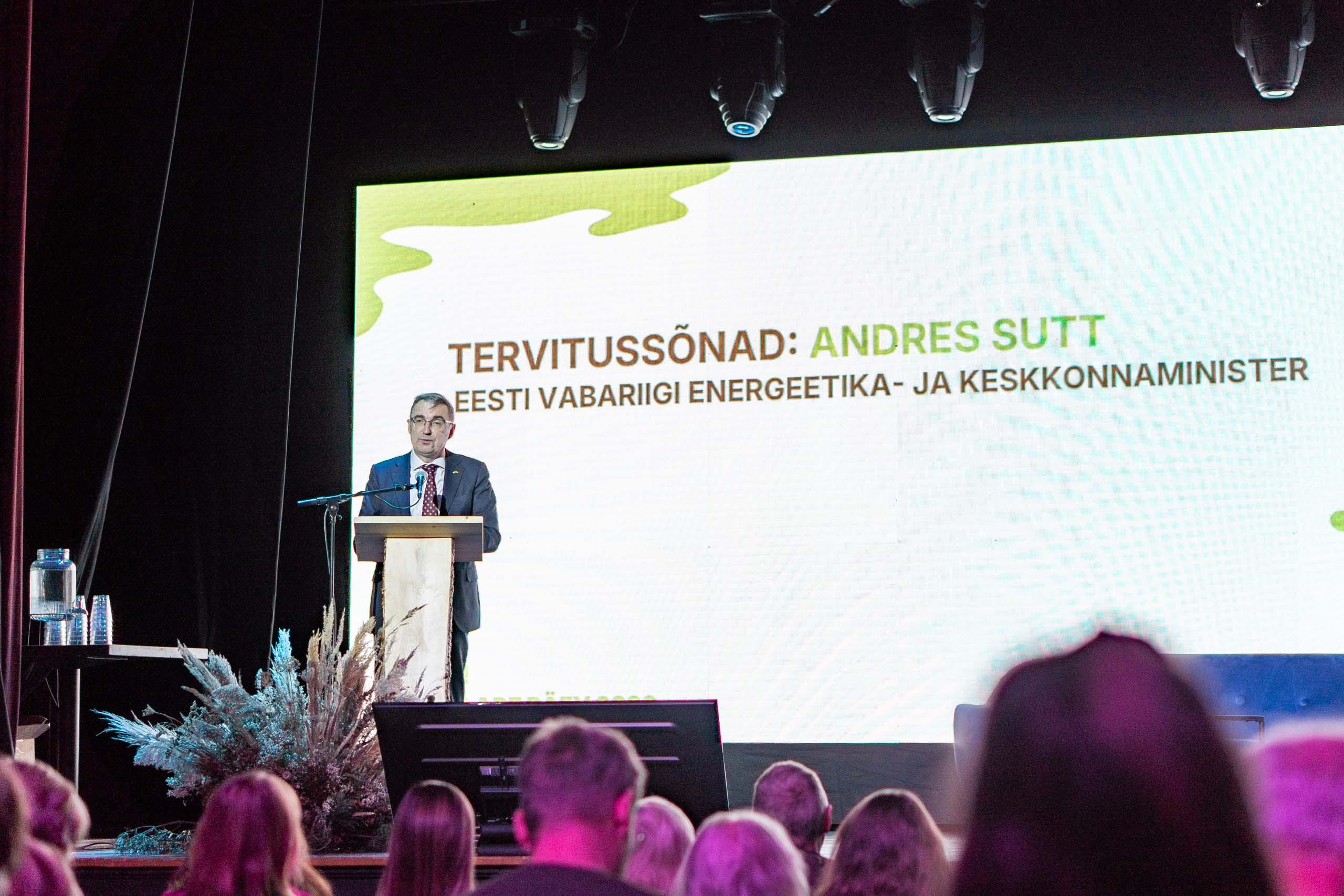 inimene konverentsil esinemas, taustal suur ekraan ja pealtvaatajad